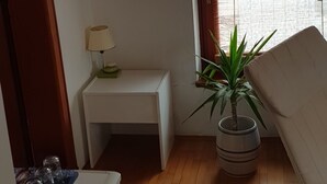 A small, well-lit room with a wooden floor, a white desk with a lamp, a potted plant, and a window with curtains. - Cozy Studio Retreat in Vrnjacka Banja (Vrnjacka Banja)