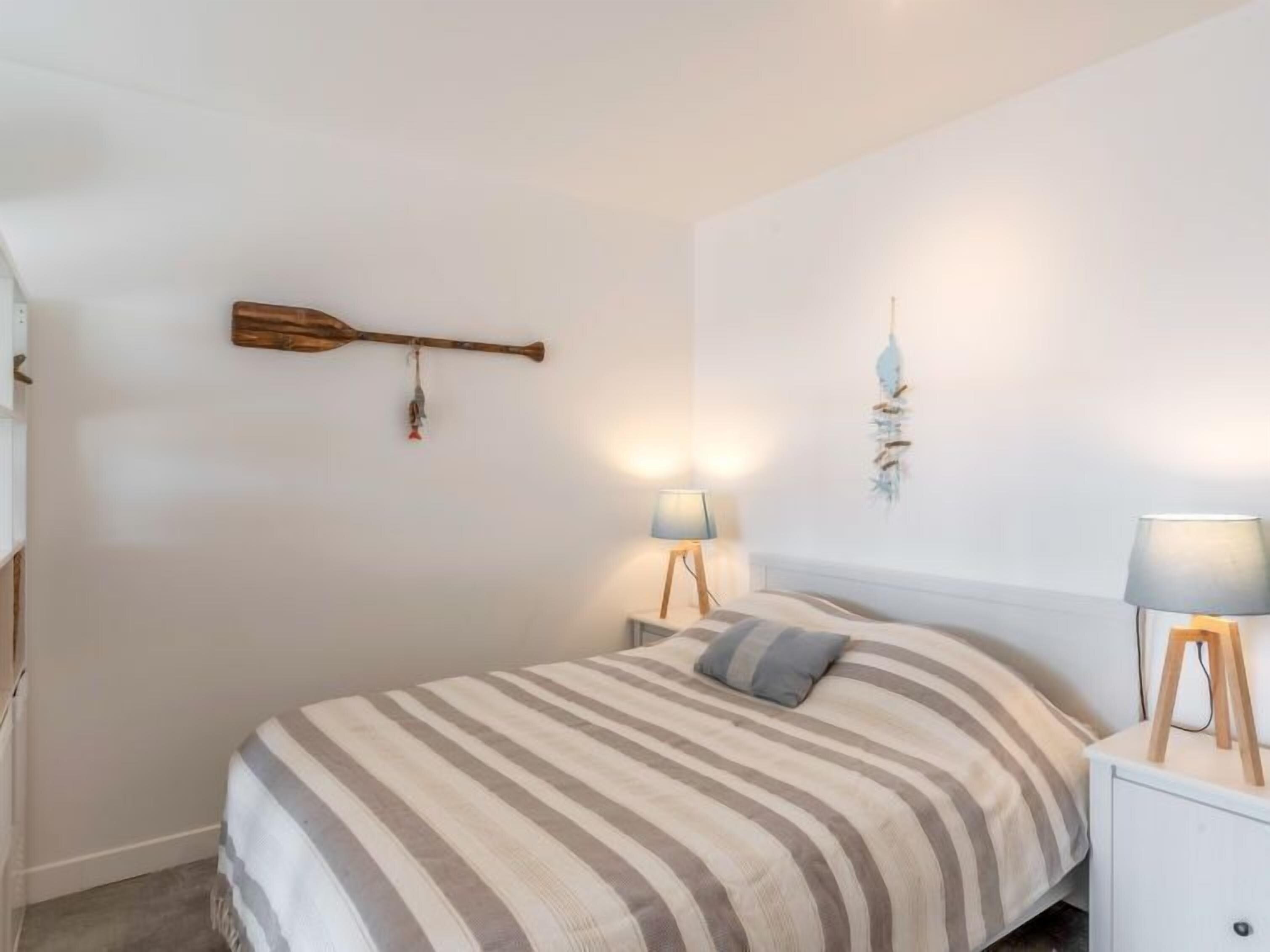 Une chambre à coucher comprenant un lit, deux tables de chevet avec des lampes, un objet en bois fixé au mur et un élément décoratif mural.