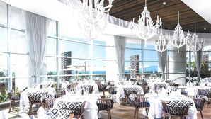 Un restaurante con varias mesas dispuestas para comer, ventanas amplias que ofrecen vistas, y candelabros colgando del techo.