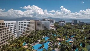 Un resort con varias construcciones, un amplio espacio de piscina y vista al mar.