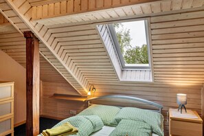 Un dormitorio con techo inclinado, tragaluz, cama con ropa de cama verde, lámpara de noche y mesita de noche de madera.