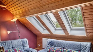 Een gezellige kamer met een houten plafond, een blauwe bank met kleurrijke kussens en dakramen.