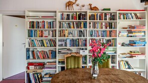 Een kamer met een grote boekenkast vol boeken, een houten tafel met een bloevas, en een groene stoel.