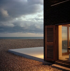 A modern building with a glass door and a concrete platform leading to a pebble beach.