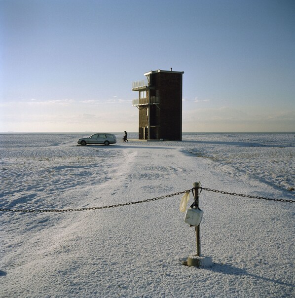 A snow-covered beach with a building in the background and a chain-link fence in the foreground.