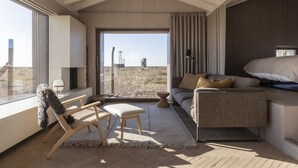 A modern room with a large window, a sofa, a chair, and a small table. - Radar by Bloom Stays - sleeps 4 on nature reserve (Dungeness)