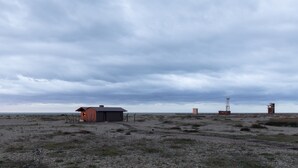 A remote, open landscape with a small, single-story building and two tall structures in the distance. - Radar by Bloom Stays - sleeps 4 on nature reserve (Dungeness)