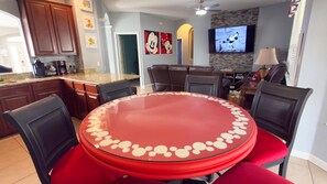Un comedor con mesa y sillas rojas, una cocina con armarios de madera, un televisor en la pared y un ventilador de techo.