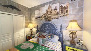 Une chambre avec un mur en pierre, un lit recouvert d’une couverture verte, deux lampes de chevet et un tableau représentant un château, accroché au mur.