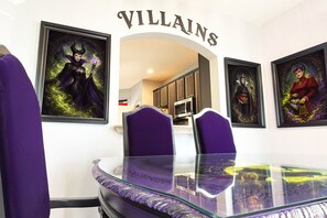 A dining area with a glass table, purple chairs, and framed artwork on the walls.
