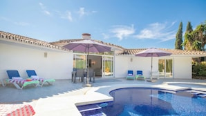 A swimming pool with lounge chairs and umbrellas, a covered patio area, and a clear blue sky. - Pool Villa Rancho Domingo family friendly, Benalmádena, Spain (Benalmádena)