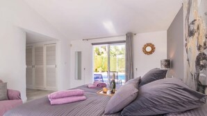 A bedroom with a bed, pillows, a tray with a bottle and glasses, and a view of a pool. - Pool Villa Rancho Domingo family friendly, Benalmádena, Spain (Benalmádena)