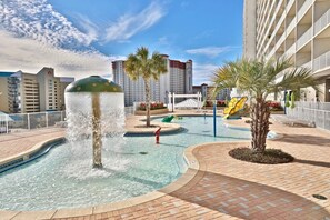 Una piscina con una fuente, palmeras y un edificio con balcones al fondo.