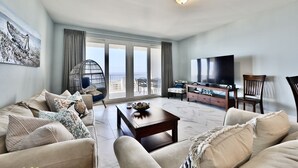 Ein geräumiges Wohnzimmer mit einer Sofagarnitur, einem Couchtisch, einem Fernseher und einem Balkon mit Blick.