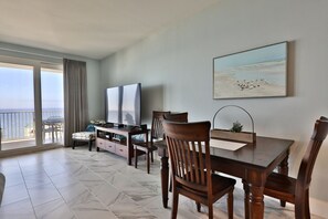 Un comedor con una mesa, sillas y un televisor. Hay un balcón con vista al océano.