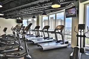 Une salle de sport équipée de tapis de course, de vélos elliptiques et d’un écran de télévision diffusant une chaîne d’information.