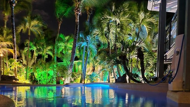A nighttime pool area with palm trees and a building in the background. - Luxury Private Villa 8–16 Guests | Lagoon Pool, Jacuzzi | Orient Bay - SXM (Baie Oientale)