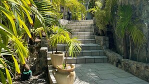 A tropical garden with palm trees, stone steps, and large planters. - Luxury Private Villa 8–16 Guests | Lagoon Pool, Jacuzzi | Orient Bay - SXM (Baie Oientale)