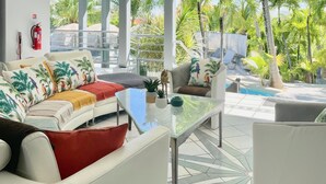 A modern outdoor living area with a white sofa, a glass coffee table, and a pool in the background. - Luxury Private Villa 8–16 Guests | Lagoon Pool, Jacuzzi | Orient Bay - SXM (Baie Oientale)