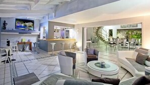 A modern living room with a TV, seating area, and a spiral staircase leading to a dining area. - Luxury Private Villa 8–16 Guests | Lagoon Pool, Jacuzzi | Orient Bay - SXM (Baie Oientale)