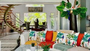 A modern living room with a sofa, coffee table, and decorative plants. - Luxury Private Villa 8–16 Guests | Lagoon Pool, Jacuzzi | Orient Bay - SXM (Baie Oientale)