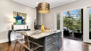 A modern kitchen with a marble island, a hanging light fixture, and a large window with a view of trees. - Yourcation® Awaits in Majestic Mountain Home! (Fairview)