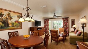 A dining area with a round table, chairs, a bowl of fruit, a television, and a ceiling fan. - Beautiful updated Condo in World Class Resort Near Disney (Orlando)
