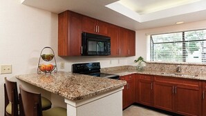 A kitchen with granite countertops, wooden cabinets, a black microwave, and a built-in oven. - Beautiful updated Condo in World Class Resort Near Disney (Orlando)