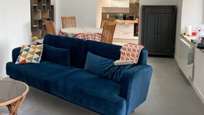 Una sala moderna con un sofá azul, una zona de comedor con una mesa y sillas, y una cocina con armarios y encimera.