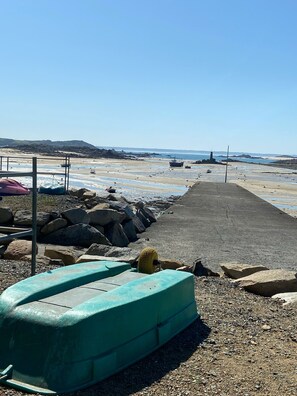 Ein felsiger Strand mit einer Betonpromenade, ein Leuchtturm in der Ferne und ein grünes Boot im Vordergrund.