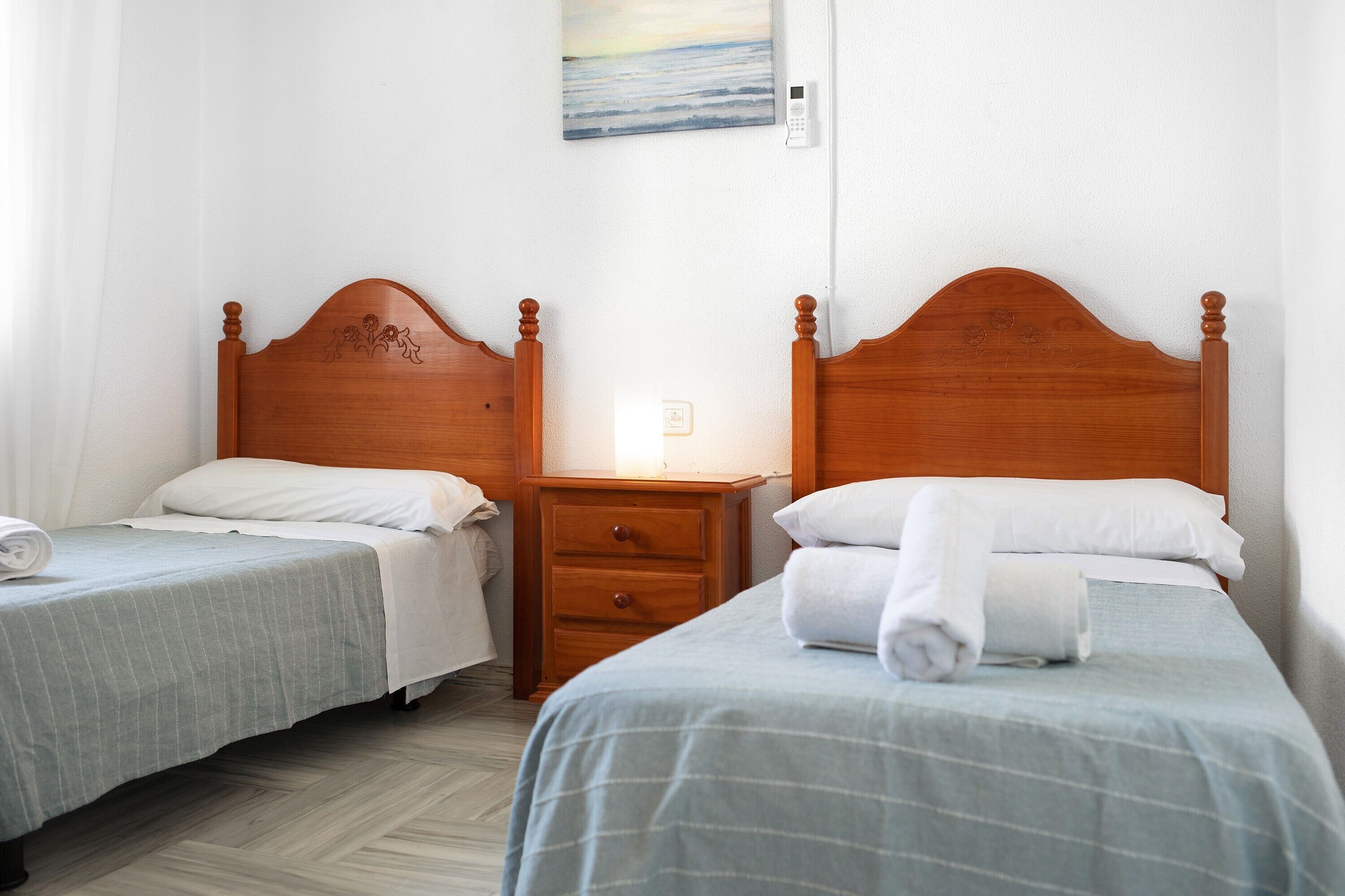 Two twin beds with wooden headboards, a bedside table, a wall-mounted thermostat, and a painting above the beds.