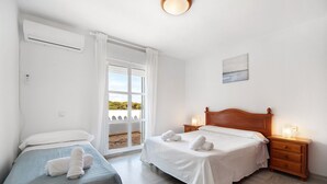 Ein Hotelzimmer mit zwei Betten, einem großen Fenster mit Vorhängen, einem Nachttisch mit Lampe und einem Gemälde an der Wand.