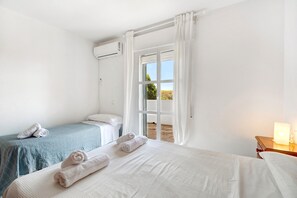 Hotellihuone, jossa on kaksi sänkyä, ikkuna, jossa on verhot, yöpöytä lampun kanssa ja ilmastointilaite seinällä.