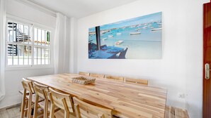 Ein Essbereich mit einem Holztisch und Stühlen, einem Bild von Booten auf dem Wasser und einem Fenster mit Vorhängen.