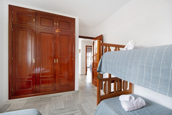 Una habitación con un armario grande de madera, una cama con colcha azul a rayas y una toalla blanca sobre la cama.