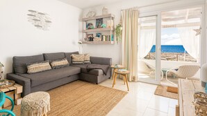 Una sala de estar con un sofá gris, una mesita redonda y vista a la playa a través de un ventanal.