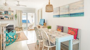 Amplia habitación con mesa de comedor, sillas, sofá, ventilador de techo y vista al mar.