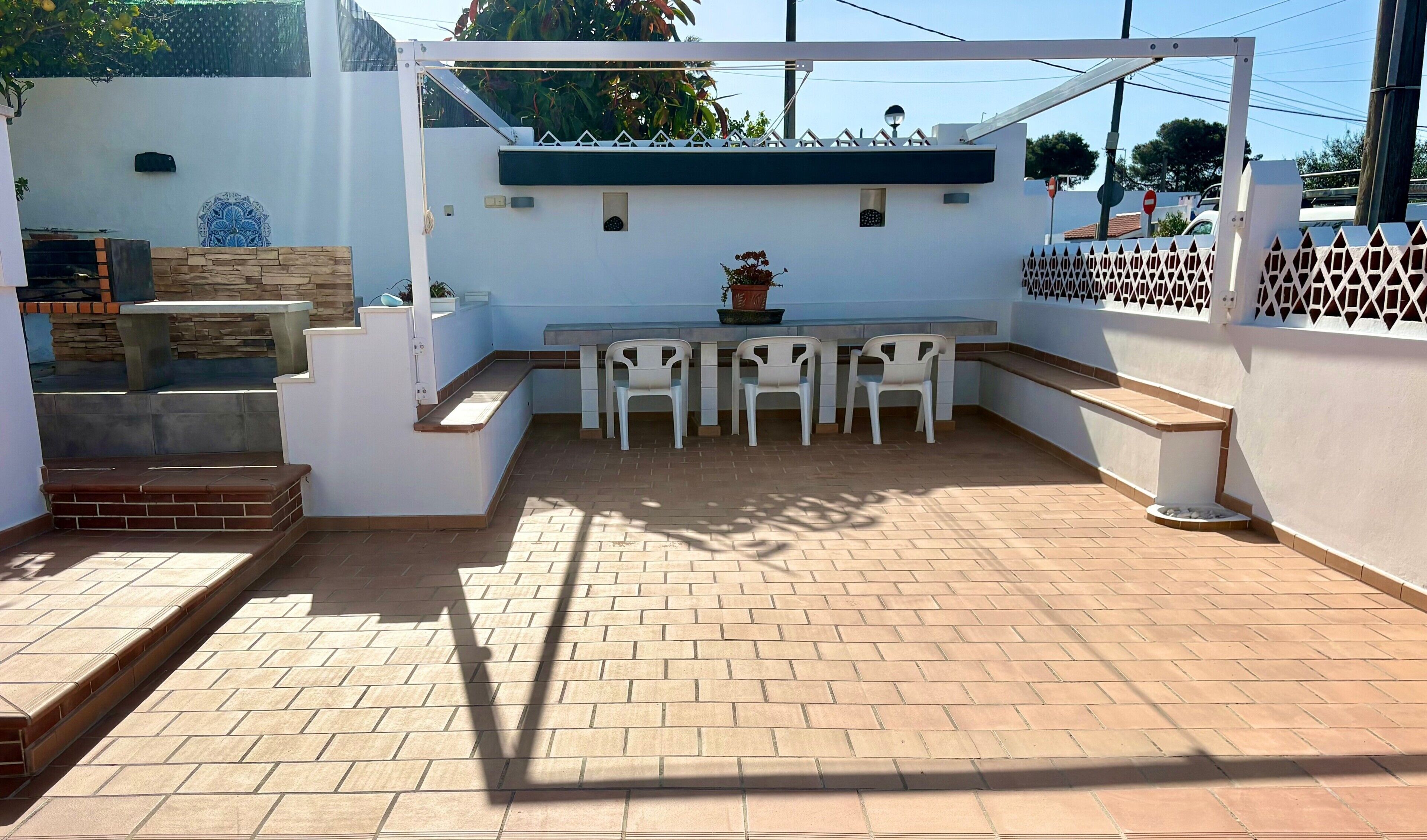 Un patio con mesa y sillas, un pequeño jardín y una pared blanca con azulejos decorativos.