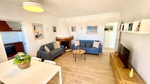 Een woonkamer met een bank, een bijzettafeltje, een open haard en een televisie.