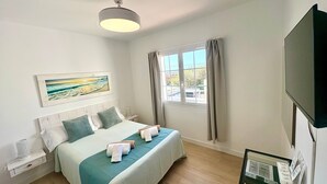 Hotelkamer met een bed, een flatscreen televisie, een raam met gordijnen, een schilderij aan de muur en een tafeltje met een afstandsbediening.