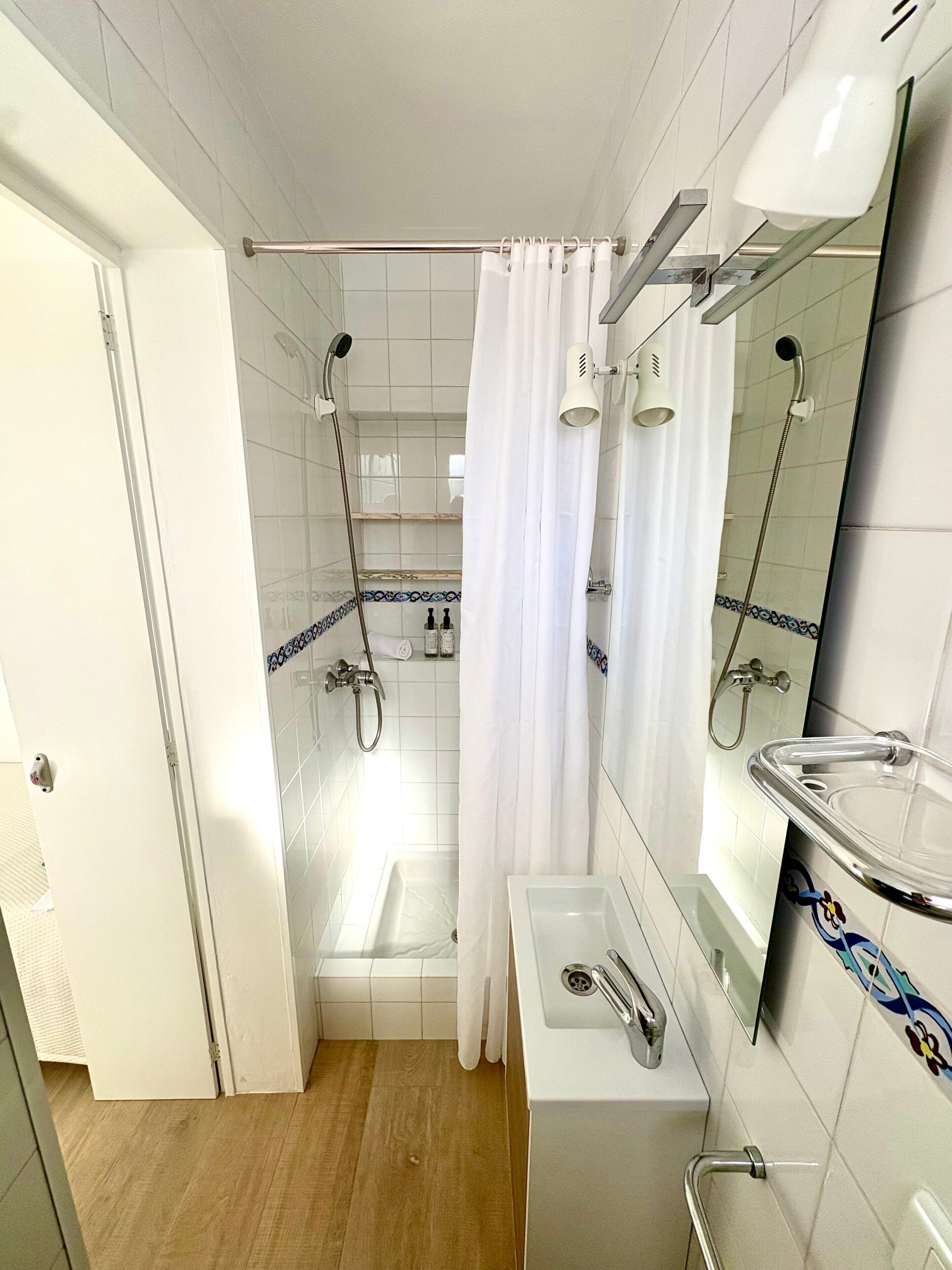 Un baño con ducha, lavabo, espejo y puerta.