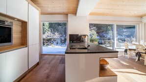 Une cuisine moderne avec un plafond en bois, de grandes fenêtres et un coin repas avec des chaises.