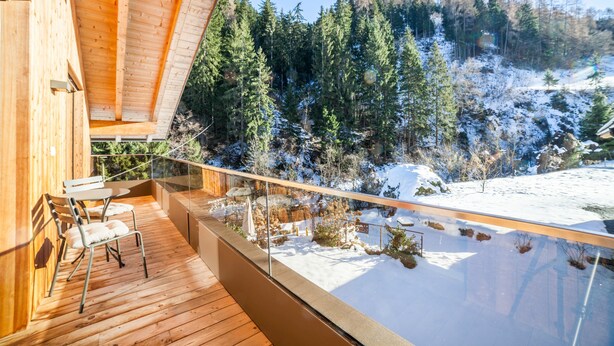 Une terrasse en bois dotée d’une balustrade en verre, offrant une vue sur un paysage enneigé et boisé.