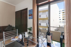 Une chambre d’hôtel avec un balcon, une table à manger avec des chaises, un canapé, une plante en pot et une bouteille de vin.