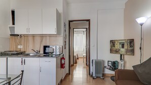 Ett kompakt bostadsutrymme med ett litet kök, en matplats, ett element och en lampa.