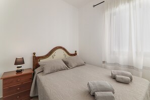 A bedroom with a bed, a nightstand, a lamp, and a window with curtains.