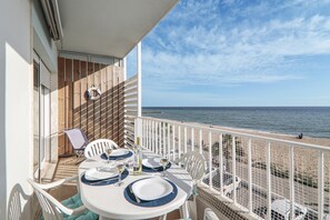 Ein Balkon mit Esstisch, der Blick auf einen Strand gewährt.