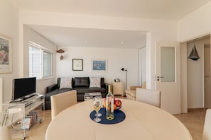 Un salon avec un téléviseur, une table à manger avec une bouteille et des verres, un canapé et une bibliothèque.