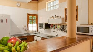 A kitchen with a wooden countertop, a microwave, a sink, and a window with curtains. - Vacation Home "Elvira Hermigua" with Sea View, Mountain View, Terraces & Garden (Hermigua)