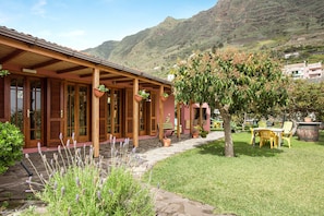 A building with a covered patio, potted plants, and a grassy area with a tree. - Vacation Home "Elvira Hermigua" with Sea View, Mountain View, Terraces & Garden (Hermigua)